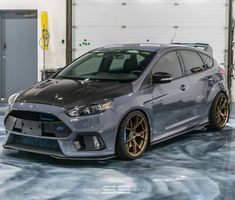 a grey car parked in a garage with yellow rims and gold accents on it