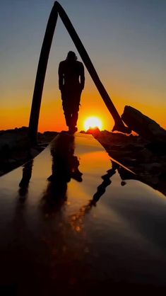 the silhouette of a person standing on top of a surfboard in front of an orange and blue sky