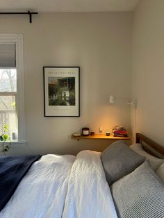 a bed sitting under a window next to a wooden table with a lamp on it