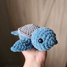 a hand holding a blue and gray stuffed turtle with its head turned to the side