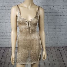 a mannequin wearing a gold dress on a wooden floor next to a brick wall