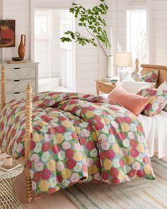 a bedroom with white walls and flooring has a bed covered in colorful bedspread