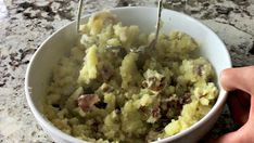 a bowl filled with mashed potatoes on top of a granite counter next to a hand