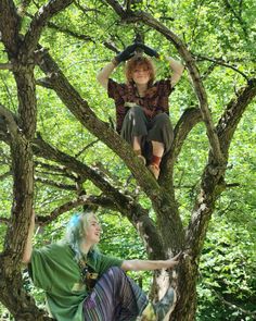 two women sitting in the branches of a tree, one on top of another woman's head