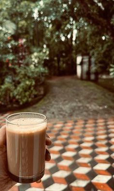 a hand holding a drink in front of a checkerboard floored area with trees