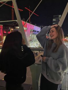 two women standing next to each other in front of a ferris wheel at night time