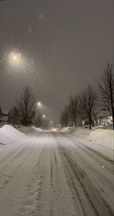 a snow covered street at night with the lights on and trees in the distance,