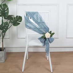 a white chair with a blue sash and flower on it in front of a potted plant