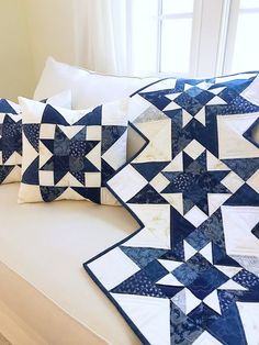 two blue and white quilted pillows sitting on a couch in front of a window