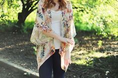 a woman standing in the woods with her hand on her hip and wearing a floral kimono