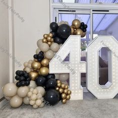 the number forty is made out of balloons and black, gold and white colors in front of a window