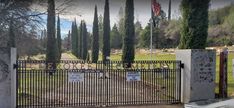 an iron gate with signs on it in front of trees and gravestones at the entrance to a cemetery