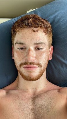 a man with freckled hair and beard laying on a blue pillow looking at the camera