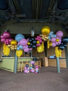 balloons and streamers are hanging from the ceiling in an open area with tables, chairs and stools