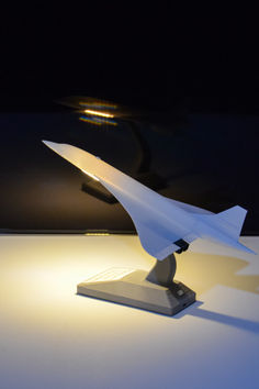 a paper airplane sitting on top of a white table next to a light that is turned on