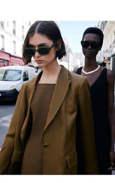 two women walking down the street with sunglasses on their head and one wearing a brown coat