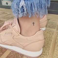 a woman's foot with a small cross tattoo on her left ankle and pink sneakers