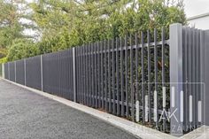 a long metal fence is next to some trees and bushes on the side of the road