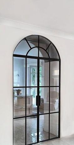 an arched glass door in the middle of a living room with white walls and tile flooring