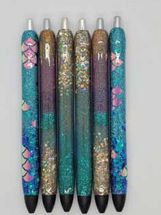 four different colored pens are lined up next to each other on a white surface with blue, green and pink glitters