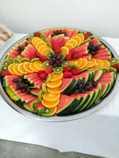 a platter filled with sliced up fruit on top of a white table next to bread