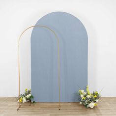 an arch with flowers on the floor next to it and a blue wall in the background