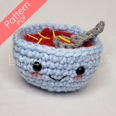 a crocheted bowl with a smiling face and spoon in it, sitting on a white surface