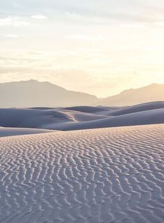 the sun shines on sand dunes in the distance, with mountains in the background