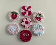 four crocheted coasters with fruit and flowers on them, all decorated in different colors