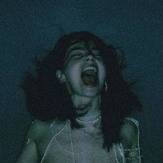 a woman with her mouth open in the dark, wearing chains and choker necklaces