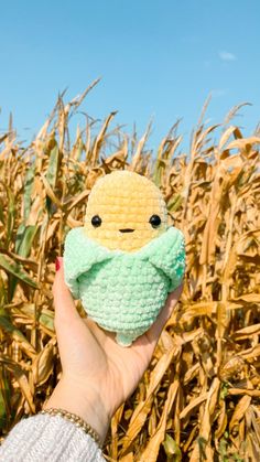 a hand holding a small toy in front of a corn field