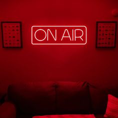 a red neon sign that reads on air above a couch in a room with pillows