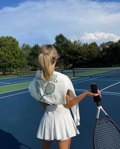 a woman holding a tennis racquet on top of a tennis court with trees in the background