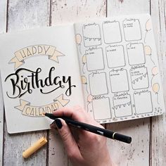 a hand holding a marker next to an open birthday planner on top of a wooden table