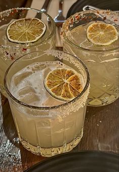 three glasses filled with lemonade sitting on top of a wooden table