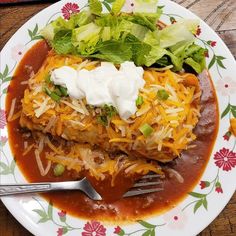 a white plate topped with tacos and sauce on top of a wooden table next to a fork