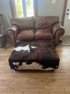 a brown and white cowhide ottoman sitting on top of a hard wood floor next to a leather couch