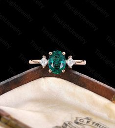 an emerald and diamond ring sitting on top of a wooden box with a black background