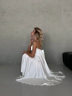 a woman in a white dress sitting on the floor with her hand under her chin