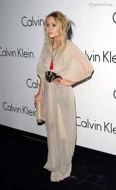 a woman standing in front of a wall wearing a dress and holding a handbag