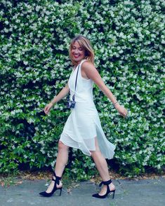 a woman in a white dress is walking down the street with her hand on her hip