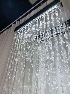 a chandelier hanging from the ceiling in front of a window with white curtains