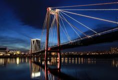 a bridge that is lit up at night with lights on it and reflecting in the water