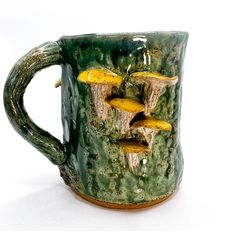 a green ceramic mug with yellow mushrooms on the outside and inside, sitting on a white surface