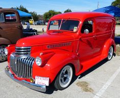 an old red truck parked in a parking lot next to other antique cars and trucks