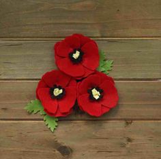 three red felt flowers with green leaves on top of wooden planks and one has a white heart in the center