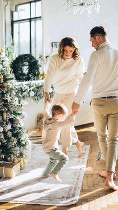 a woman and man holding hands as a toddler stands on a rug in front of a christmas tree