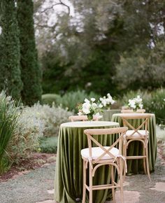 an outdoor dining area with green tablecloths and chairs, surrounded by greenery