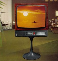 an old television sitting on top of a black pedestal in front of a window with the sun setting behind it