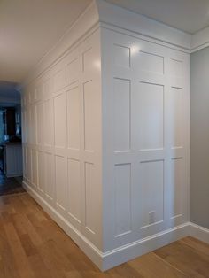 an empty room with white paneling and wood floors